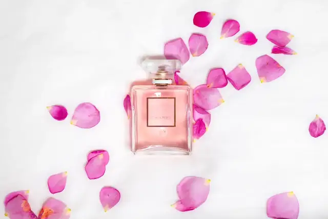 Perfumy Chanel Coco Mademoiselle w różowym flakonie otoczone płatkami róż na białym tle.