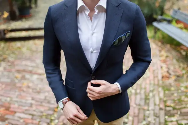 Mężczyzna w granatowej marynarce, białej koszuli i z poszetką w kratę.