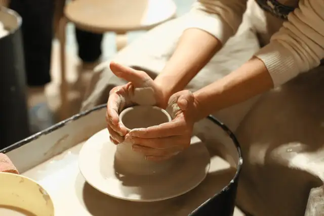 Ręce formują glinę na kole garncarskim podczas zajęć z ceramiki.