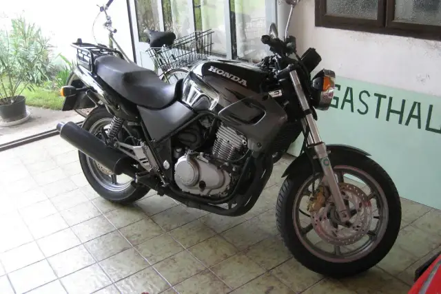 Czarny motocykl Honda z widocznym silnikiem i wydechem, gotowy do jazdy. Obok stoi rower.