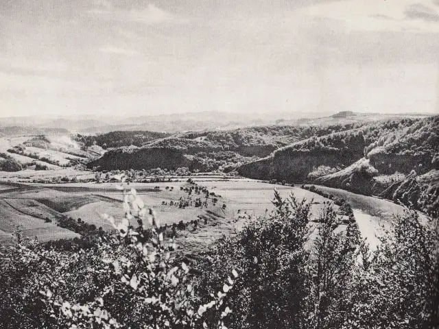 Krajobraz z doliną rzeki, polami i zalesionymi wzgórzami.