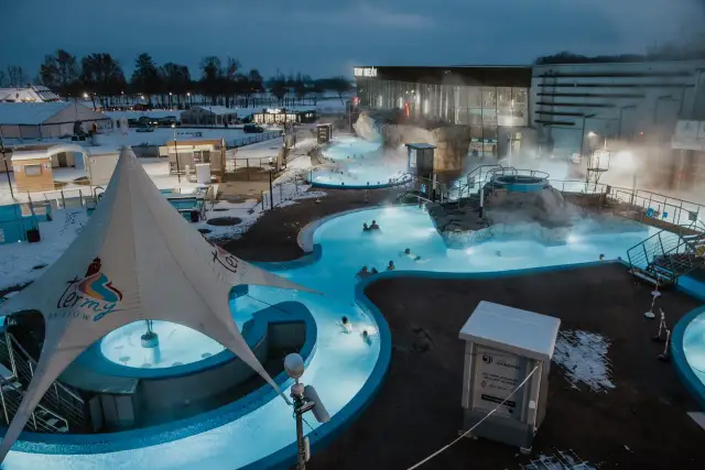 Gdzie są Termy Uniejów? W zimowy wieczór ludzie relaksują się w podgrzewanych basenach zewnętrznych kompleksu.