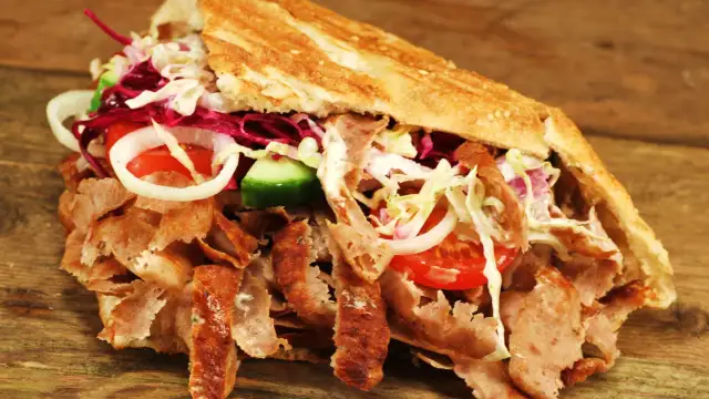 Kebab z mięsem, warzywami i sosem w bułce na drewnianym tle.