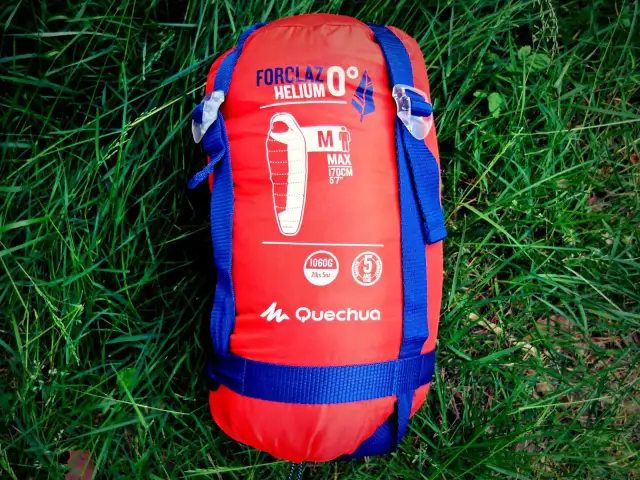 Czerwony śpiwór Forclaz Helium 0° na trawie, idealny do zapewnienia komfortu termicznego w chłodne noce.