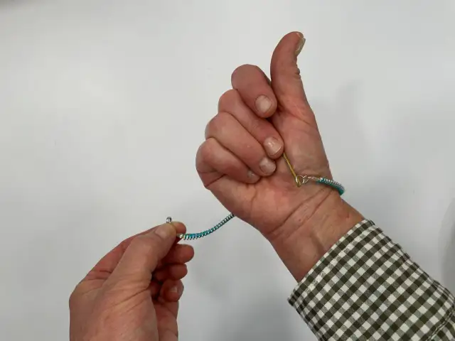 Pokazuje, jak zapiąć bransoletkę. Jedna ręka trzyma zapięcie, druga zapina je na nadgarstku.