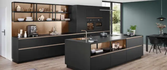 Cocina moderna con isla central, gabinetes negros, detalles dorados y electrodomésticos integrados.