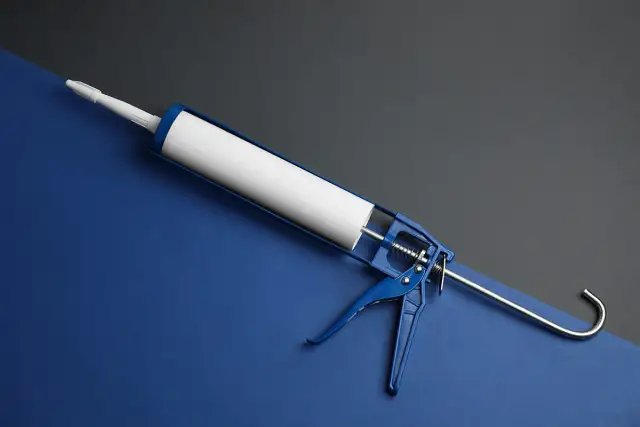 Niebieski pistolet do silikonu z białą tubą na tle dwóch kolorów.