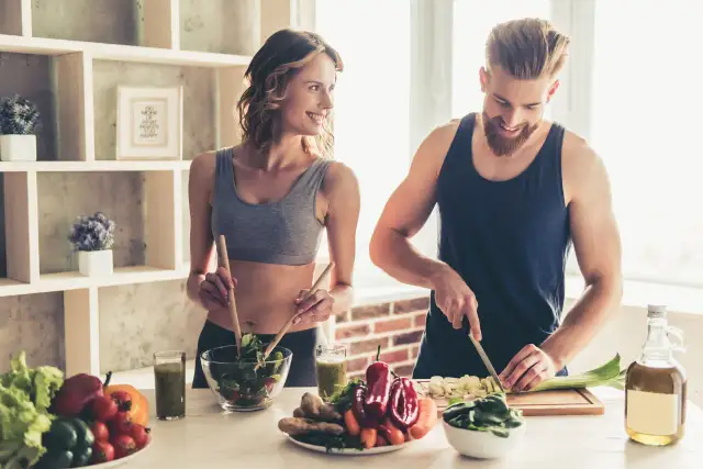 Para dieta 3000 kcal jadłospis tygodniowy, para przygotowuje zdrowe posiłki. Ona miesza sałatkę, on kroi warzywa.