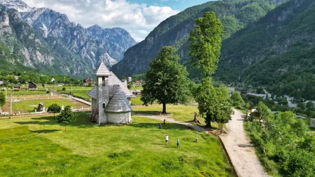 Kamienna cerkiew w Theth, Albania, otoczona zielonymi wzgórzami i majestatycznymi górami.