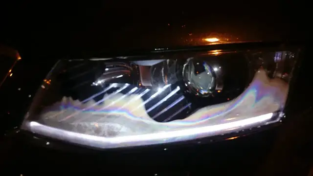 Parujące reflektory LED w nowym aucie, z tęczowymi refleksami na mokrej powierzchni.