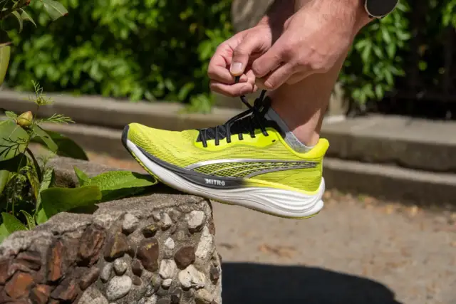 Dłoń wiąże sznurówki jaskrawożółtego buta Puma Deviate Nitro 3, gotowego na bieg.