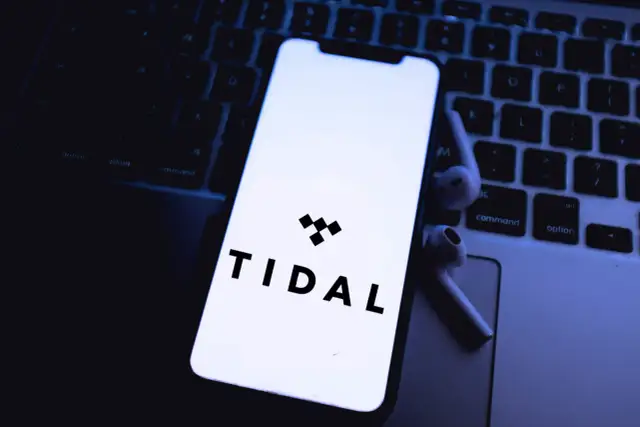 Smartfon z logo Tidal na klawiaturze laptopa i słuchawkami bezprzewodowymi.