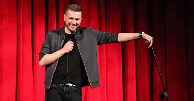 Mateusz Socha na scenie z mikrofonem, na tle czerwonej kurtyny.