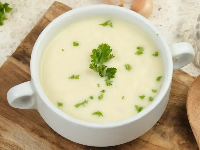 Biała miseczka z kremową zupą, udekorowana natką pietruszki, na drewnianej desce.