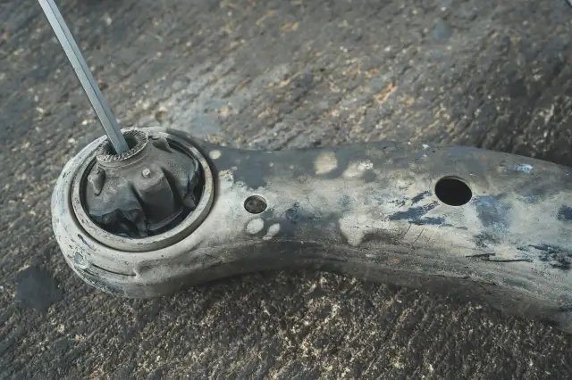 Metalowy pręt włożony w zniszczony gumowy element wahacza. To pokazuje, jak sprawdzić sworzeń wahacza.