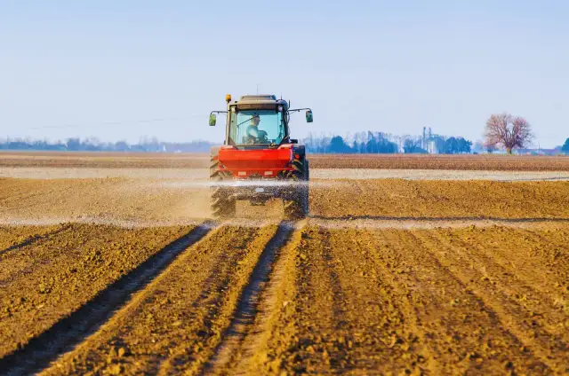 Czerwony traktor rozsiewa wapno z magnezem na polu, przygotowując ziemię do nowego sezonu.
