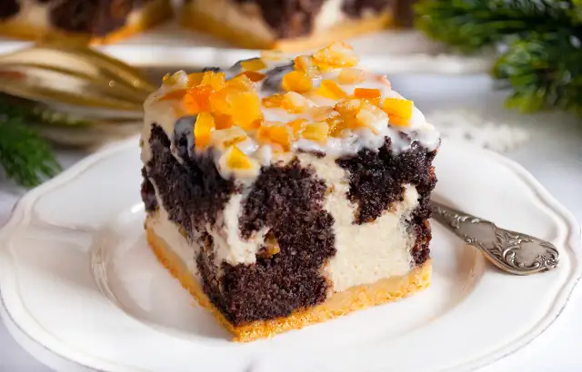 Pyszny sernik z makiem, udekorowany kandyzowaną skórką pomarańczową, na białym talerzyku.