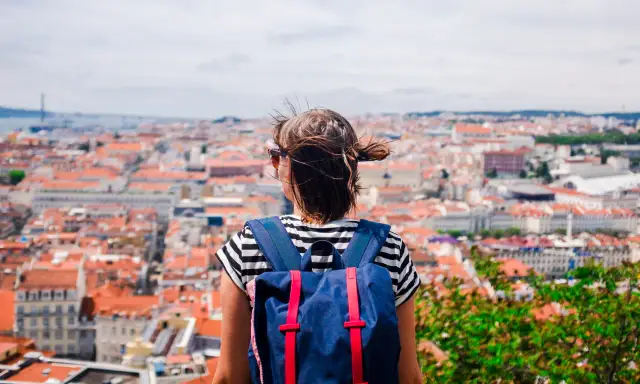 Widok zza pleców osoby z plecakiem na miasto z czerwonymi dachami.