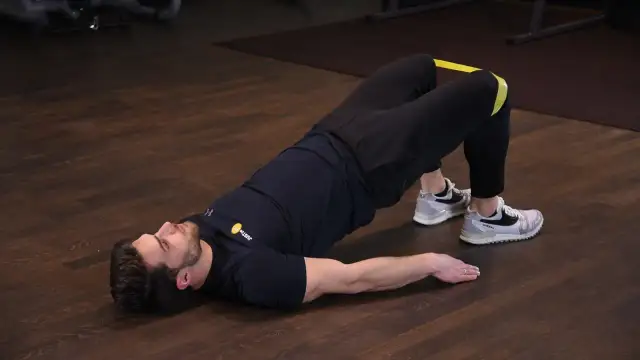 Mężczyzna wykonuje ćwiczenie glute bridge z gumą na udach, napinając pośladki.