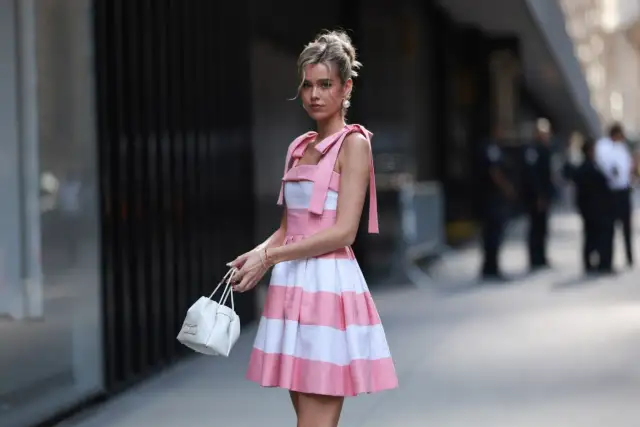 Dziewczyna w różowo-białej sukience w paski, z kokardkami na ramionach, trzyma białą torebkę. To kwintesencja stylu coquette.