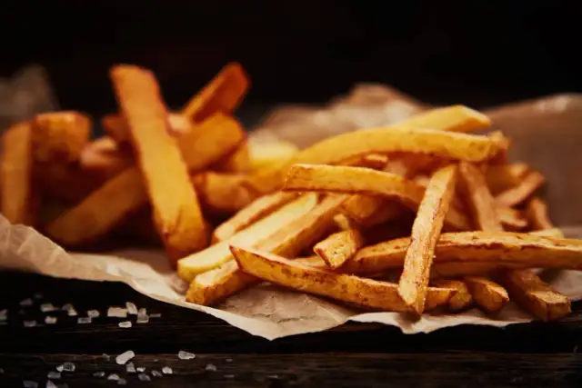 Złociste, chrupiące frytki domowe ułożone na papierze, z widoczną solą na drewnianym tle.