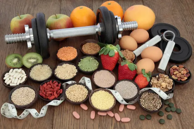 Hantle, owoce, jajka, nasiona i suplementy diety na drewnianym tle.