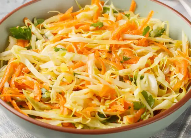 Surówka z białej kapusty i marchewki z natką pietruszki w misce.