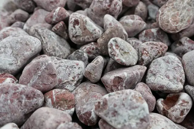Zbliżenie na stos zaokrąglonych, różowo-szarych kamieni, używanych jako kruszywo.