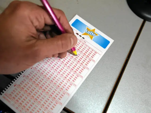 Dłoń z różowym ołówkiem zaznacza liczby na kuponie Lotto.