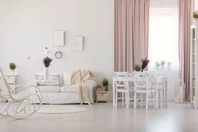 Jasny salon w stylu prowansalskim. Biała kanapa, fotel bujany, stół z krzesłami i lawenda tworzą przytulną atmosferę.