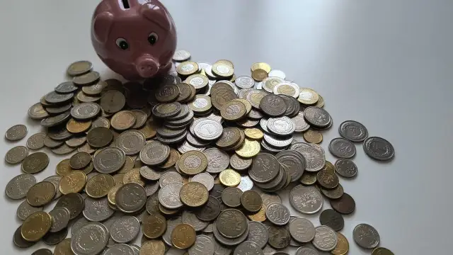Różowa świnka-skarbonka i stos monet. Zastanawiasz się, ile kosztuje konsultacja u prawnika? Może warto zacząć oszczędzać?
