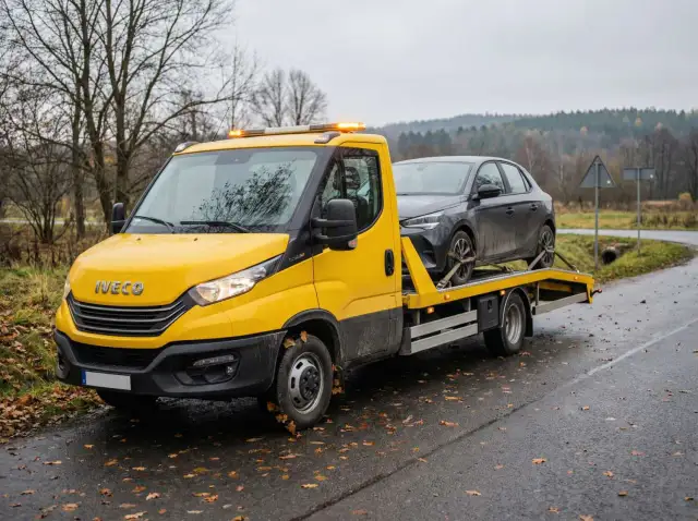 Żółta laweta Iveco z ciemnym samochodem na platformie. Zastanawiasz się, ile kosztuje laweta?