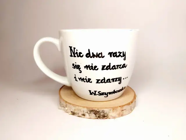 Biały kubek z cytatem Wisławy Szymborskiej: "Nic dwa razy się nie zdarza i nie zdarzy...". Wczoraj kiedy twoje imię ktoś wymówił przy mnie głośno wiersz.