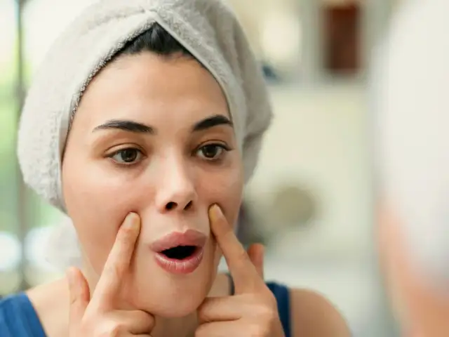 Kobieta z ręcznikiem na głowie ćwiczy jogę twarzy, dbając o skórę po 60 roku życia.