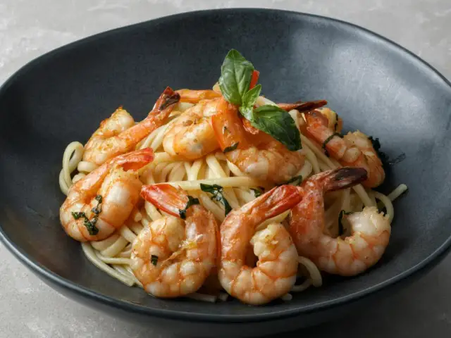 Pyszne dania z krewetkami na talerzu: makaron z soczystymi krewetkami i listkami bazylii.