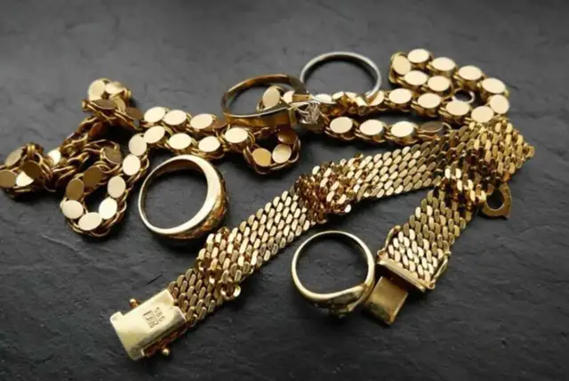 Złota biżuteria: naszyjnik, bransoletki i pierścionki na ciemnym tle.