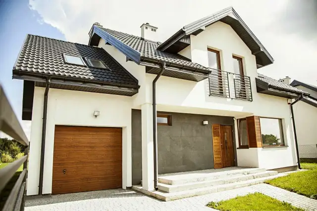 Nowoczesny dom z grafitowym dachem, białymi ścianami i drewnianą bramą garażową.