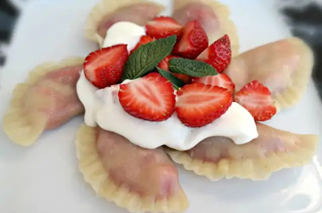 Pyszne pierogi z truskawkami, polane śmietaną i ozdobione świeżymi owocami i miętą. Letnia uczta na talerzu.