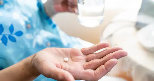 Dłoń trzyma białą tabletkę, przygotowując się do połknięcia. Zrozumienie aspiryna działanie to klucz do ulgi w bólu.