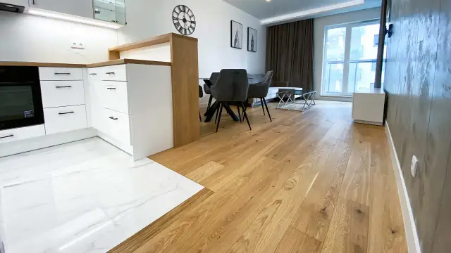Eleganckie łączenie podłogi drewnianej z płytkami w nowoczesnym wnętrzu. Drewniana podłoga płynnie przechodzi w białe płytki z marmurowym wzorem.