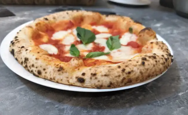 Pizza Margherita na białym talerzu, z widocznym puszystym brzegiem i świeżą bazylią.