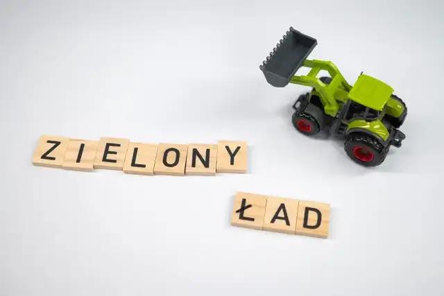 Drewniane klocki z literami "ZIELONY ŁAD" i zielona zabawka koparka na białym tle.