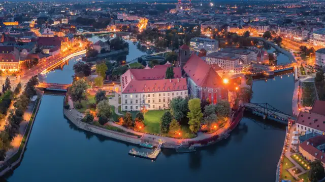 Ostrów Tumski we Wrocławiu nocą, z oświetlonymi budynkami i rzeką. To jedno z najpiękniejszych miejsc Wrocławia.