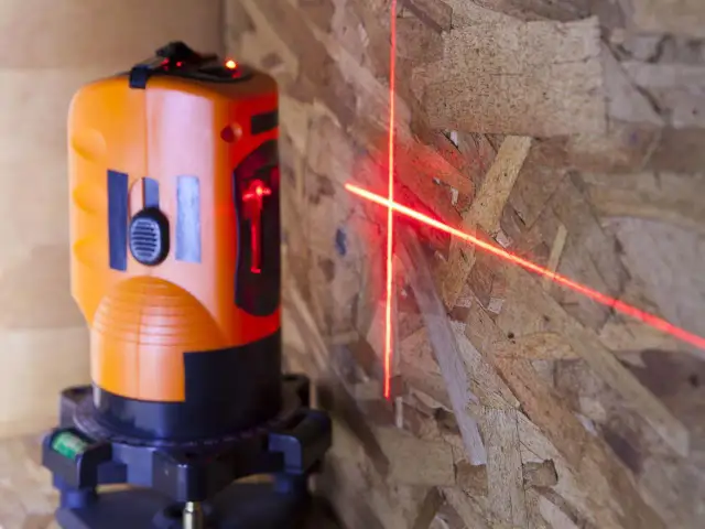 Pomarańczowa poziomica laserowa emituje czerwone linie na drewnianej ścianie.