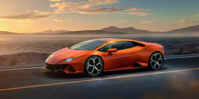 Pomarańczowy Lamborghini Huracan pędzi po pustej drodze nad jeziorem o zachodzie słońca.