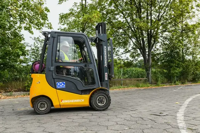 Operator w kasku i kamizelce prowadzi wózek widłowy Jungheinrich. Zastanawiasz się, ile kosztuje uprawnienia na wózek widłowy?