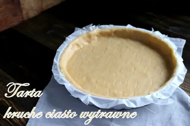 Surowe ciasto kruche wytrawne na tartę, przygotowane do pieczenia. Widelcem nakłute dno i boki.