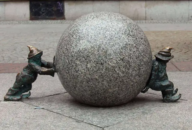 Dwa wrocławskie krasnale pchają kamienną kulę. Ile jest krasnali we Wrocławiu? Tyle, ile potrzeba do wspólnego celu!