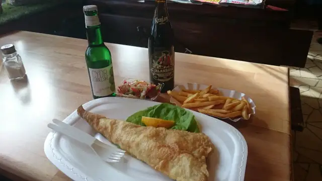 Smażona ryba z frytkami, surówką i napojami na drewnianym stole.