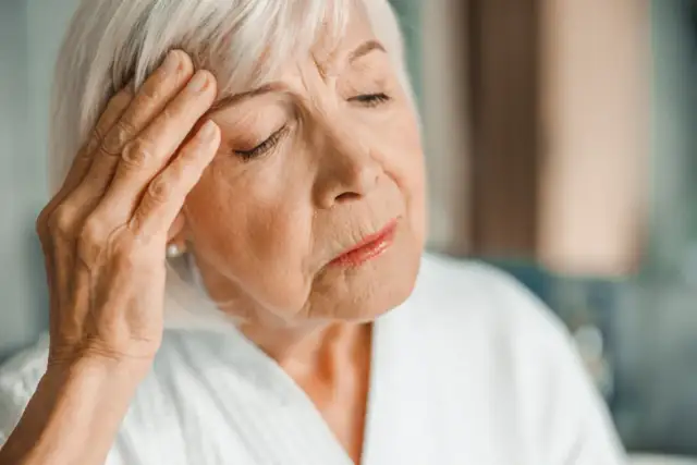Starsza kobieta z ręką na skroni, zamyślona. Może to być jeden z objawów choroby Alzheimera.